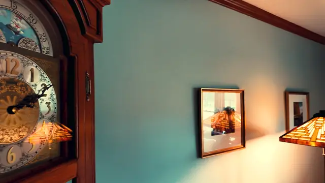 The face of a grandfather clock beside a framed print, lit by a stained-glass lamp