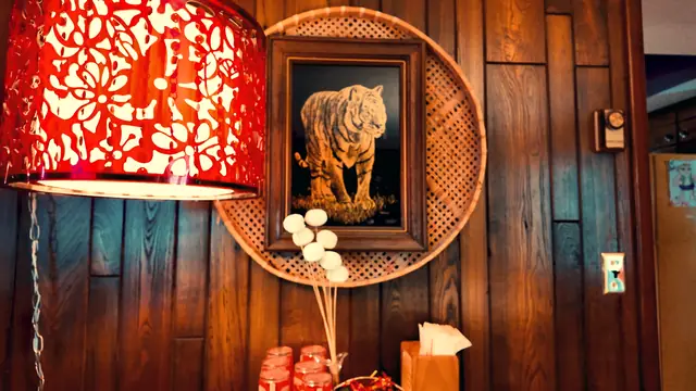 A red pierced-metal pendant lamp beside a framed tiger print on wood paneling
