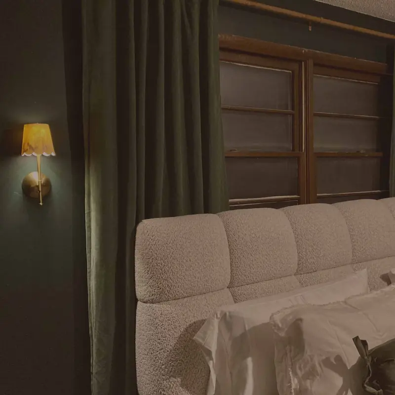 Moody bedroom with a brass sconce and deep green curtains