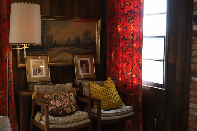 Living room corner with curated art, a floor lamp and bold red curtains