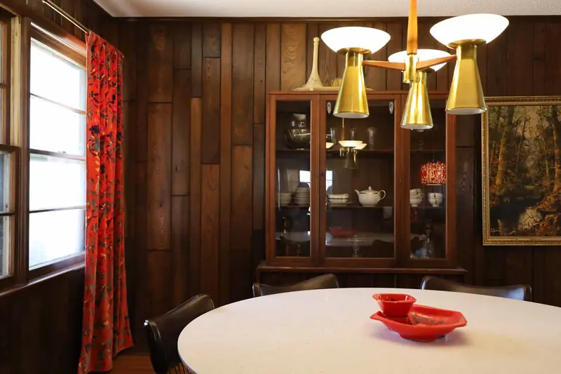 Dining room with a brass chandelier, china cabinet and red floral curtains