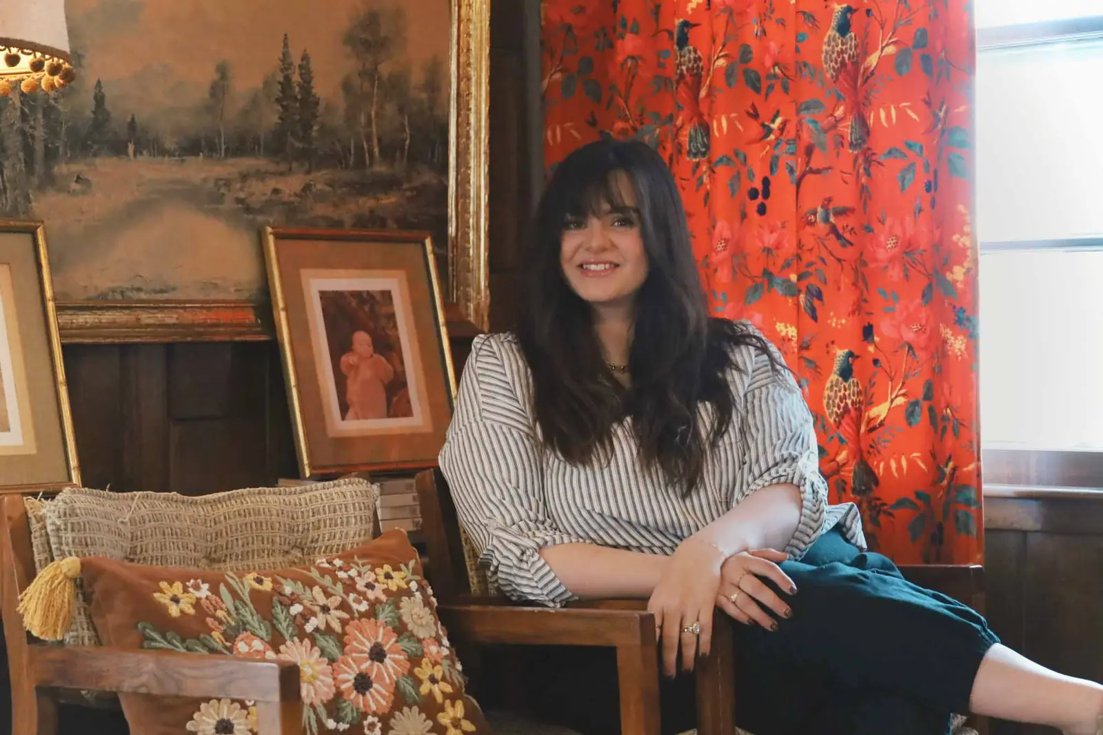 Sarah Stewart sitting in a wood-paneled room with red floral curtains and vintage framed art